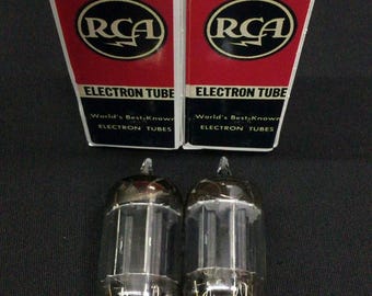 May include: Two RCA 12AU7 Radiotron electron tubes in their original red, white, and black rectangular cardboard boxes. The boxes feature the RCA logo, the text 12AU7, Radiotron, and Electron Tube. The glass tubes have visible internal metal components.