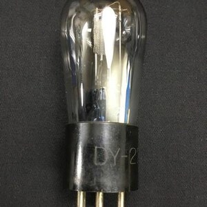 Puede incluir: Una válvula de vacío vintage con una bombilla de vidrio transparente y una base negra. La base tiene tres pines y el texto "DY-23" impreso. Los componentes internos son visibles a través del vidrio.