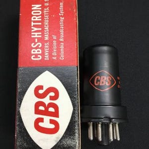 May include: Vintage CBS-HYTRON vacuum tube and box. The box is red and black with the CBS logo in white and red. The tube is black with the CBS logo in a red diamond. The box reads "DANVERS, MASSACHUSETTS, U.S.A."