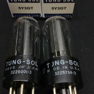 May include: Two Tung-Sol 5Y3GT electron tubes with clear glass envelopes and black bases, each featuring white text reading Tung-Sol Made in U.S.A. and a serial number. They are positioned in front of their original white and blue cardboard boxes.