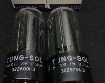 May include: Two Tung-Sol 5Y3GT electron tubes with clear glass envelopes and black bases, each featuring white text reading Tung-Sol Made in U.S.A. and a serial number. They are positioned in front of their original white and blue cardboard boxes.