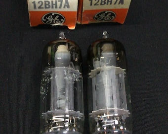 May include: Two clear glass vacuum tubes with internal metal components and pins at the base, accompanied by two orange and white General Electric boxes labeled 12BH7A. The boxes feature the GE logo and the text Electron tube.