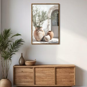 May include: A framed print of three terracotta pots with a green plant in the largest pot. The pots are sitting on a white patio with a white door in the background.