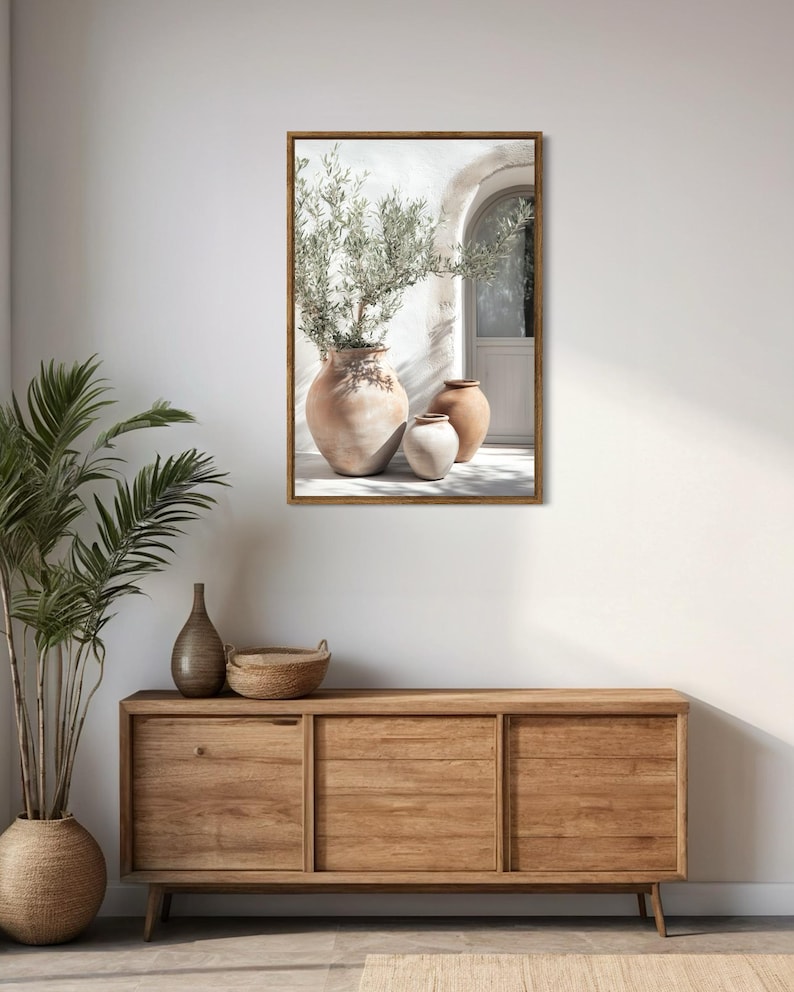 May include: A framed print of three terracotta pots with a green plant in the largest pot. The pots are sitting on a white patio with a white door in the background.