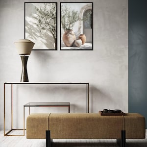 Puede incluir: Una escena de dise&ntilde;o de interiores con dos estampados bot&aacute;nicos enmarcados, una l&aacute;mpara de mesa, una consola, una peque&ntilde;a mesa auxiliar y un banco. El banco est&aacute; tapizado en tela color beige y tiene patas negras. Los estampados representan ramas de olivo y jarrones.