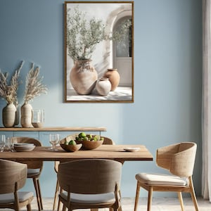 May include: A framed print of a whitewashed wall with an arched doorway and three terracotta pots with green plants. The pots are arranged in a row, with the largest pot in the center and the two smaller pots on either side. The print is hung on a light blue wall in a dining room with a wooden table and chairs.