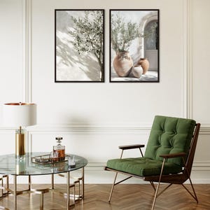 Puede incluir: Dos impresiones art&iacute;sticas enmarcadas con ramas de olivo en jarrones, exhibidas en una pared blanca. Una mesa de centro redonda de cristal con base dorada, un sill&oacute;n verde y una l&aacute;mpara dorada completan la decoraci&oacute;n.