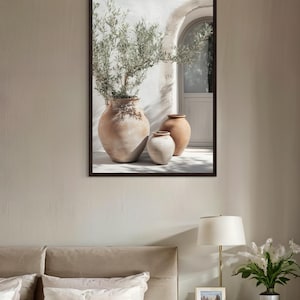 May include: A framed print of a white wall with an arched doorway and three terracotta pots. The pots are arranged in a row, with a small olive tree in the largest pot. The print has a rustic and minimalist aesthetic.