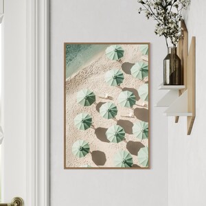 May include: An aerial view of a beach with rows of green umbrellas and their shadows on the sand.