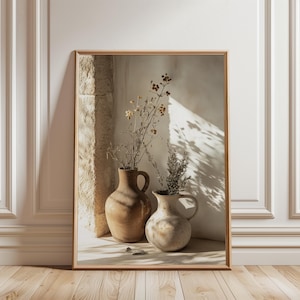 May include: A framed print depicting two earthenware vases holding dried flowers. The vases are in shades of brown and beige, set against a neutral wall with a stone architectural feature. The artwork is framed in light wood.
