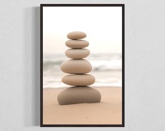 May include: A stack of smooth, light brown stones balanced on top of each other on a sandy beach. The stones are arranged in a pyramid shape, with the largest stone at the bottom and the smallest stone at the top.