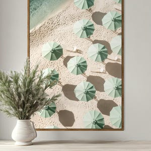 May include: An aerial view of a beach with rows of light green umbrellas on the sand. The umbrellas are arranged in a grid pattern, with their shadows cast on the sand.