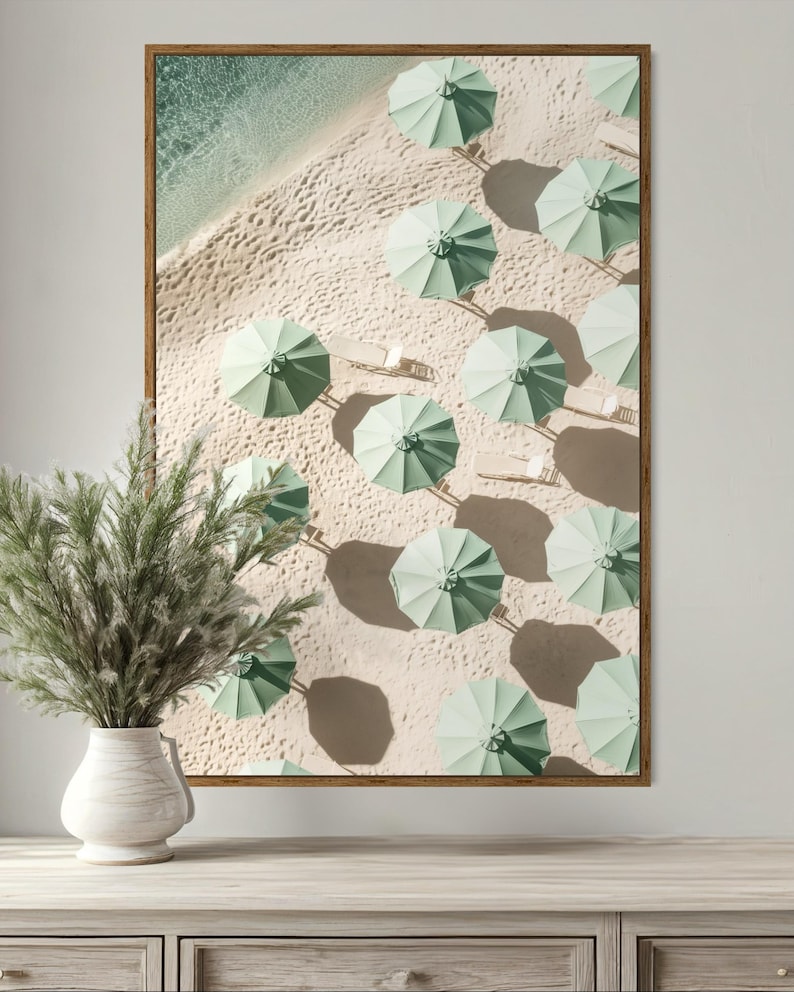 May include: An aerial view of a beach with rows of light green umbrellas on the sand. The umbrellas are arranged in a grid pattern, with their shadows cast on the sand.