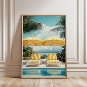 以下が含まれることがあります： 黄色と白のストライプのラウンジチェアとマッチするパラソルが2つあるプールサイドのシーンを描いた、額入りのアートプリント。このアートワークは、ヤシの木、プール、青い空の下の海の景色がある穏やかな海岸の風景を描いています。