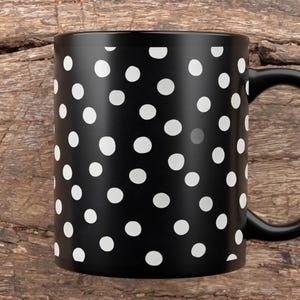 May include: A black ceramic mug with a white polka dot pattern. The mug has a black handle and is set against a rustic wooden background. This coffee mug is perfect for hot beverages.