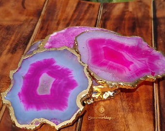 May include: A stack of agate coasters with a vibrant pink and white pattern, edged with gold trim. The coasters are displayed on a dark wooden surface, showcasing their natural beauty and unique design.