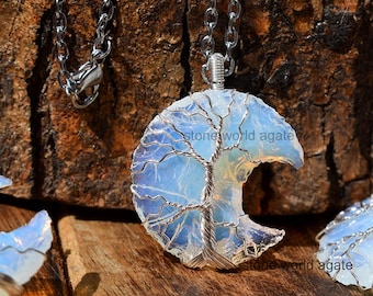 May include: A silver chain necklace with a pendant featuring a crescent moon design. The moon is made of a light blue, opalescent stone with a wire tree design. The text "stonesworld agate" is visible on the pendant.