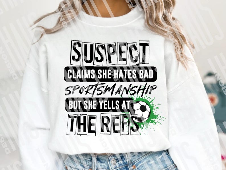 Pode incluir: Camisola branca com o texto "SUSPECT CLAIMS SHE HATES BAD SPORTSMANSHIP BUT SHE YELLS AT THE REFS" em letras pretas. Um gr&aacute;fico de bola de futebol com respingos de tinta verde est&aacute; &agrave; direita.