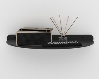May include: A black half-circle shelf mounted on a white wall. The shelf holds a black speaker with a gold phone on top, a black remote control, and a glass jar with sticks.