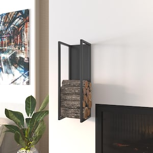 May include: A black metal firewood holder mounted on a white wall, filled with stacked logs. The holder has a rectangular frame design. The logs are brown and have a rough texture. A painting and a plant are in the background.