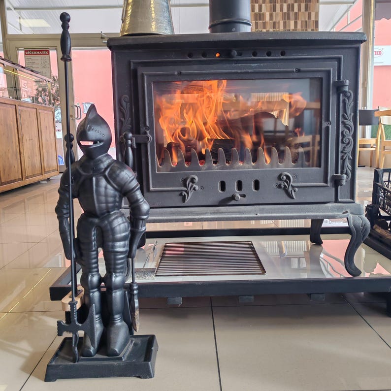 Cast iron fireplace tool set with a knight statue stand, displayed near a burning fireplace for a cozy ambiance.