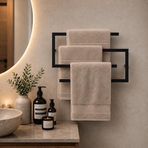May include: A matte black metal towel rack with a geometric frame design, holding three folded beige towels. The rack is mounted on a textured wall, providing a structured storage solution for bathroom linens in a neutral color palette.