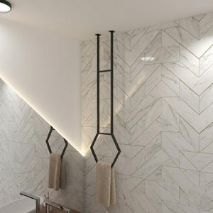 May include: Two black metal towel racks with geometric designs are mounted on a marble-patterned wall. Each rack holds a beige towel. The bathroom has a modern, minimalist design.