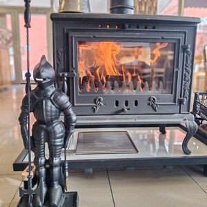 Cast iron fireplace tool set with a knight statue stand, displayed near a burning fireplace for a cozy ambiance.