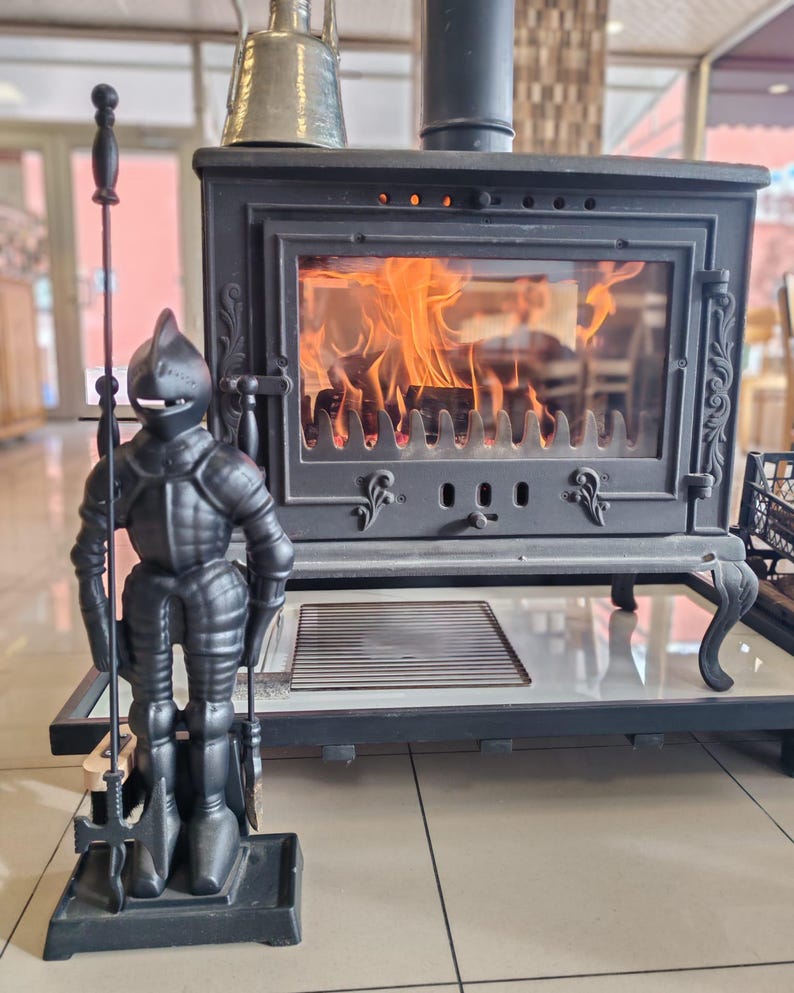 Cast iron fireplace tool set with a knight statue stand, displayed near a burning fireplace for a cozy ambiance.