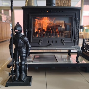 Knight-shaped fireplace tool set in cast iron, featuring a decorative medieval knight stand holding a poker, shovel, tongs, and brush, placed next to a lit fireplace.