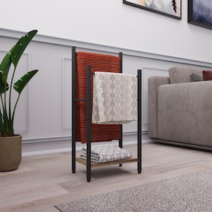 May include: A black metal blanket stand with two shelves. The stand has a red and white patterned blanket folded on top and a beige blanket folded on the bottom shelf.