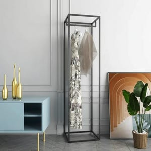 Pode incluir: Um cabide de metal preto com uma estrutura retangular. Um vestido estampado e uma peça transparente penduram-se na barra superior. Um armário azul claro com pernas douradas e garrafas douradas decorativas estão no fundo.