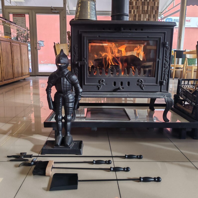 Decorative knight-shaped cast iron fireplace tool set with essential tools, standing next to a cozy, glowing wood-burning stove.