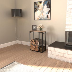 May include: A black metal and wood log holder with stacked firewood. The holder has a rectangular frame and a light-colored wood top. A framed picture and a bouquet of white flowers sit on top. A black floor lamp and a painting are in the background.