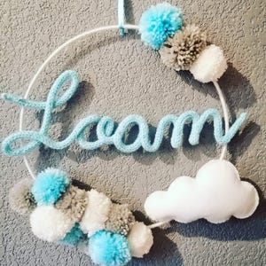 May include: A white hoop with the word "Dream" spelled out in light blue yarn. The hoop is decorated with white, gray, and light blue pom-poms and a white felt cloud.