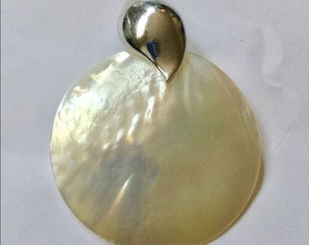 May include: A round, white mother of pearl pendant with a silver swirl design.