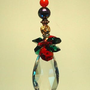 Peut inclure: Un attrape-soleil en forme de larme de cristal avec des accents de cristal rouge et vert. L'attrape-soleil est enfilé avec des perles, dont une perle rouge, une perle irisée foncée et une perle dorée.