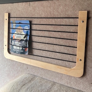 May include: A wooden shelf with a black wire grid insert. A blue and white bag of dog treats is on the shelf. The bag says "Campfire Smores Bites" and "Denzel's".
