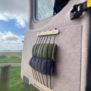 May include: A wooden towel rack with black elastic cords attached to the wood. Two towels, one green and one dark blue, are hanging on the rack.