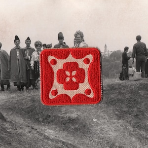 May include: A red and beige embroidered patch with a floral design. The patch is square with a red border and a beige center. The floral design is red and features a four-petal flower in the center.