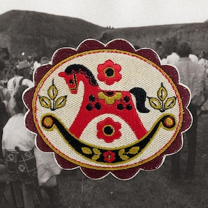 Op de afbeelding: Een geborduurde patch met een rood schommelpaardontwerp, zwarte en gele accenten en een geschulpte bordeauxrode rand. De patch is geplaatst tegen een neutrale achtergrond. Het ontwerp bevat bloemen- en bladmotieven.