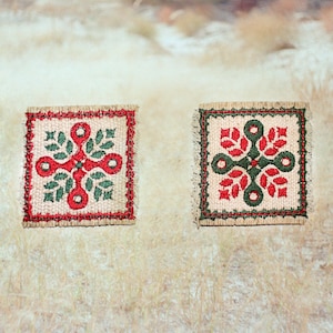 Può includere: Due toppe quadrate ricamate con bordi sfilacciati su tessuto beige chiaro. La toppa a sinistra presenta un motivo floreale a forma di croce rossa con foglie verdi. La toppa a destra mostra un motivo floreale a forma di croce verde con foglie rosse.
