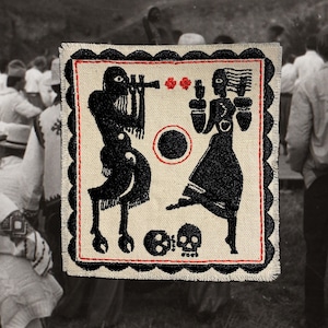Puede incluir: Parche bordado con un diseño negro y rojo sobre un fondo crema. El diseño presenta dos figuras, un círculo y dos calaveras. El parche tiene un borde festoneado y está sobre un fondo borroso en blanco y negro.