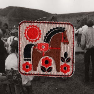 May include: Embroidered square patch with a brown horse, black mane and tail, red saddle and accents, and red flowers. The background is light beige with a red sun. The patch is outlined in red stitching.