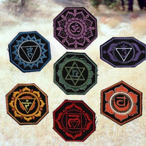 May include: Seven embroidered patches in various colors, each featuring a different chakra symbol. The patches are octagonal with black borders and intricate designs in shades of blue, purple, green, orange, and red. The background is a blurred outdoor scene.