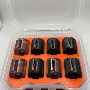 May include: A clear plastic storage case with an orange interior holds eight black and clear magazine inserts.