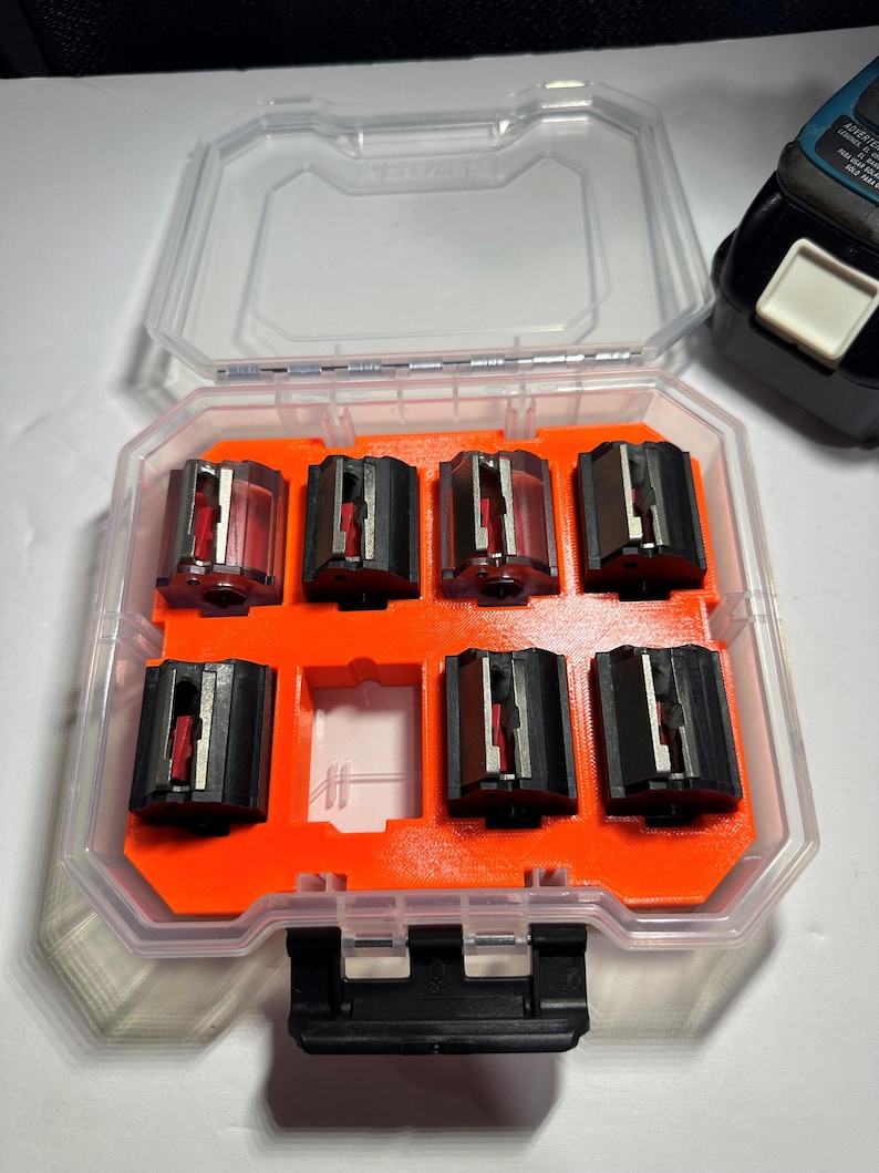 May include: A clear plastic storage case with an orange interior holds six black and red router bits. The case has a black latch on the front.