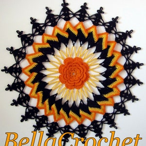 May include: A black, orange, and yellow crocheted doily with a flower in the center. The doily is circular and has a delicate lace pattern.
