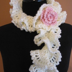 May include: A white crocheted scarf with a ruffled design and a pink crocheted flower accent.
