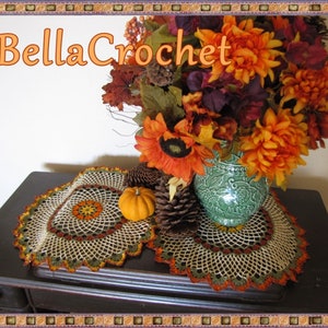 May include: A crocheted table runner with a brown, orange and green colour scheme. The runner is on a dark brown table with a vase of autumn flowers in the background. The vase is green and has a floral design. The flowers are orange, yellow and red. The text "BellaCrochet" is in the top left corner of the image.